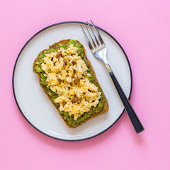 Egg on whole wheat bread with avocado, pink background top view