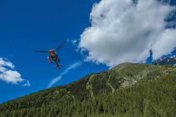 Helicopter taking off in a forest at Argentiere, a small alpine village with several ski routes in the winter and hiking in summer. Near Chamonix in the French Alps