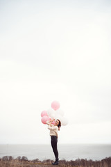 Young woman is standing on a cliff near the sea with Air balloons - 208773819