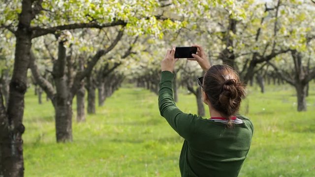 Rear view of a young caucasian woman in the nature taking photos with her smartphone