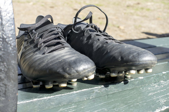 on a green park / diamond field bench a pair of used black cleats