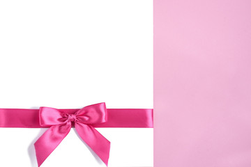 Blank paper note with pink ribbon bow on pink background.