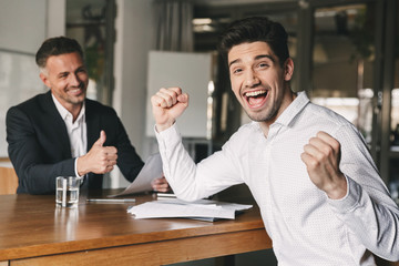 Career, office and placement concept - excited caucasian man 30s rejoicing and clenching fists...