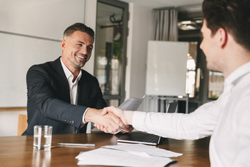 Business, career and placement concept - joyful handsome businessman 30s smiling and shaking hands...