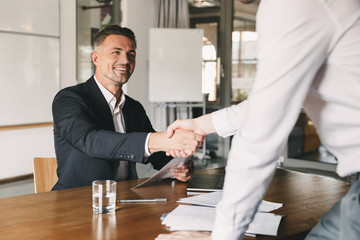 Business, career and placement concept - satisfied director man 30s smiling and shaking hands with...