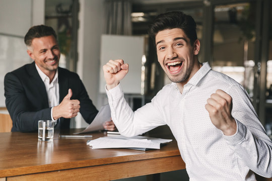Career, office and placement concept - excited caucasian man 30s rejoicing and clenching fists after job interview, since was hired for a job in big company