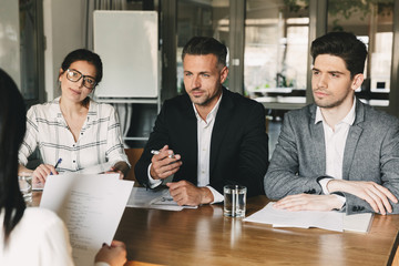 Business, career and placement concept - three executive directors or head managers sitting at table in office, and interviewing woman for job in company