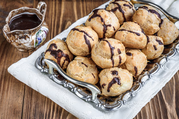 Profiteroles is a delicious culinary dishes of French cuisine with chocolate icing and nuts. Delicious profiteroles dessert on plate on dark wooden background.