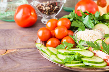 Fresh slices of cucumbers, tomatoes, sesame seeds in a bowl and parsley leaves on a plate