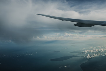 Naklejka premium Wing of airplane above island while the sun is going down with lots of clouds in the sky. Traveling concept