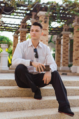 Obraz premium Young businessman holding his phone and sitting on stairs outdoors