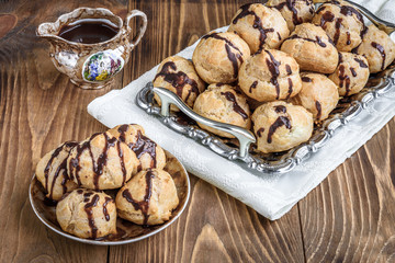 Profiteroles is a delicious culinary dishes of French cuisine with chocolate icing and nuts. Delicious profiteroles dessert on plate on dark wooden background.