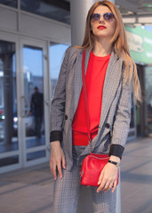 A woman with a red lipstick and a red bag in the city on the street next to the shopping center. Close-up. Street style