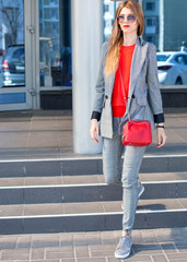 A woman with a red lipstick and a red bag in the city on the street next to the shopping center. Close-up. Street style
