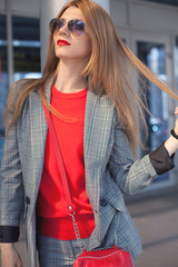 A woman with a red lipstick and a red bag in the city on the street next to the shopping center. Close-up. Street style