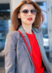 A woman with a red lipstick and a red bag in the city on the street next to the shopping center. Close-up. Street style
