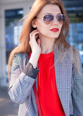 A woman with a red lipstick in the city on the street next to the shopping center. Close-up. Street style