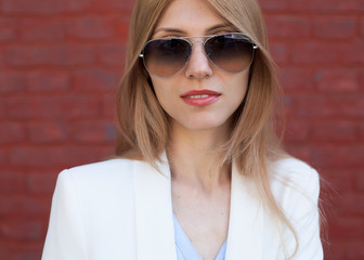 Fashion portrait of a girl with glasses and a white jacket on a red wall