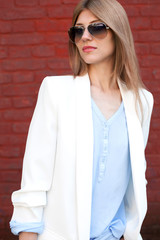 Fashion portrait of a girl with glasses and a white jacket on a red wall