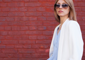 Fashion portrait of a girl with glasses and a white jacket on a red wall
