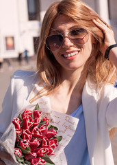 Woman in sunglasses smiling and holding flowers in the street