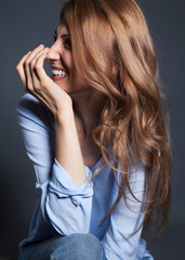 Emotional portrait of a woman in a blue blouse with long ginger hear on a gray background in a studio that laughs