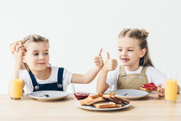 little sisters eating toasts with jam for breakfast and showing thumb up isolated on white