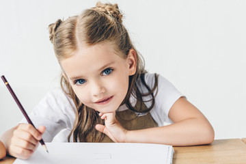 beautiful little schoolgirl drawing and looking at camera isolated on white
