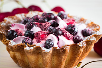 Fresh fruit and berry tart dessert with toss sugar on wooden background. Delicious sweet cake with raspberries, figs, strawberries, cherry, and cream.