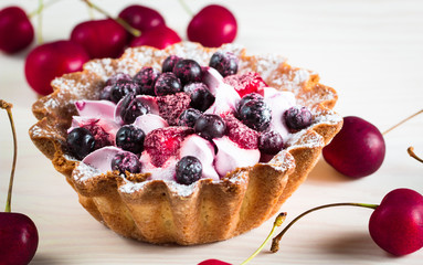 Fresh fruit and berry tart dessert with toss sugar on wooden background. Delicious sweet cake with raspberries, figs, strawberries, cherry, and cream.