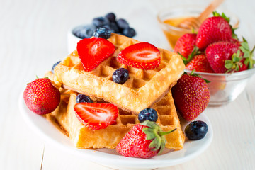 Photo of fresh homemade food made of berry Belgian waffles with honey, chocolate, strawberry, blueberry, maple syrup and cream. Healthy dessert breakfast concept with juice. 