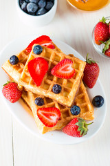 Photo of fresh homemade food made of berry Belgian waffles with honey, chocolate, strawberry, blueberry, maple syrup and cream. Healthy dessert breakfast concept with juice. 
