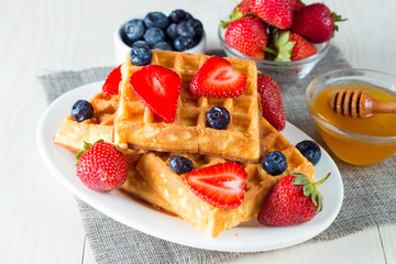 Photo of fresh homemade food made of berry Belgian waffles with honey, chocolate, strawberry, blueberry, maple syrup and cream. Healthy dessert breakfast concept with juice. 