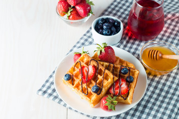 Photo of fresh homemade food made of berry Belgian waffles with honey, chocolate, strawberry, blueberry, maple syrup and cream. Healthy dessert breakfast concept with juice. 