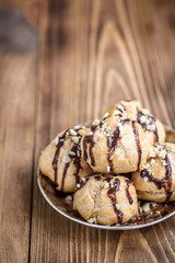 Profiteroles is a delicious culinary dishes of French cuisine with chocolate icing and nuts. Delicious profiteroles dessert on plate on dark wooden background.