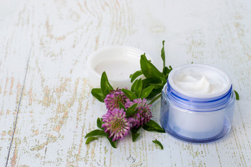 Obraz na płótnie Canvas Natural cosmetics for face and body skin care. A round jar with cream and fresh clover flowers on a light wooden background. 