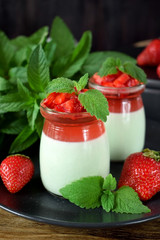 Two layered panna cotta with matcha tea topped with strawberry jelly, berries and mint in glass jars