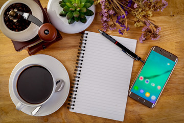 smartphone, diary, Flower, and coffee mug on wooden table.