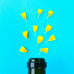 The neck of a bottle and the petals of a yellow flower on a pastel blue background.