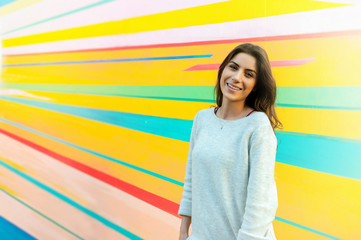Young beautiful caucasian woman posing outdoor in the city, near a colorful wall, looking at camera