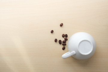 Coffee beans close to white inverted cup on wooden table, no more coffee.