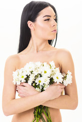 Obraz na płótnie Canvas Girl on calm face stands naked and holds chamomile flowers in front of chest. Skin health concept. Woman with smooth healthy skin looks attractive. Lady covers breasts with flowers, isolated on white.