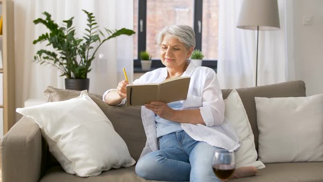 age, leisure and people concept - happy senior woman writing to notebook or diary at home