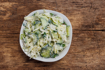 Spring salad with cabbage, cucumber, green onion, parsley and mayonnaise on wooden table