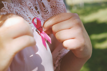 Woman hands pinning on pink breast cancer awareness ribbon.