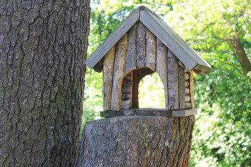 Tree House Wooden Small Handmade Birdfeeder at the Forest. Tree House and Bird Feeder Isolated on Summer Green Trees Background Close Up View. Empty Birdhouse Made from Wood Outdoors at the Park.