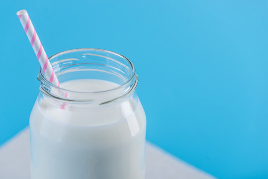 Glass bottle of fresh milk with straw on blue background. Colorful minimalism. Healthy dairy products with calcium