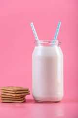Glass bottle of fresh milk with two straw and cookies on pink background. Healthy dairy products with calcium