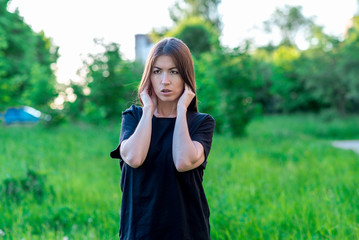 Girl summer in the park in fresh air. Hands showing a gesture closing his ears. Loud noise of...