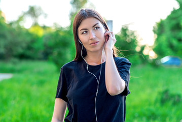Beautiful brunette girl listening to music on headphones in summer in outdoor park. Emotional looking up dreams to fantasize. Smiling positive thoughts about good